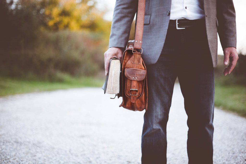 A low shot of an elegantly dressed man with a leather bag holding a Bible in his hand