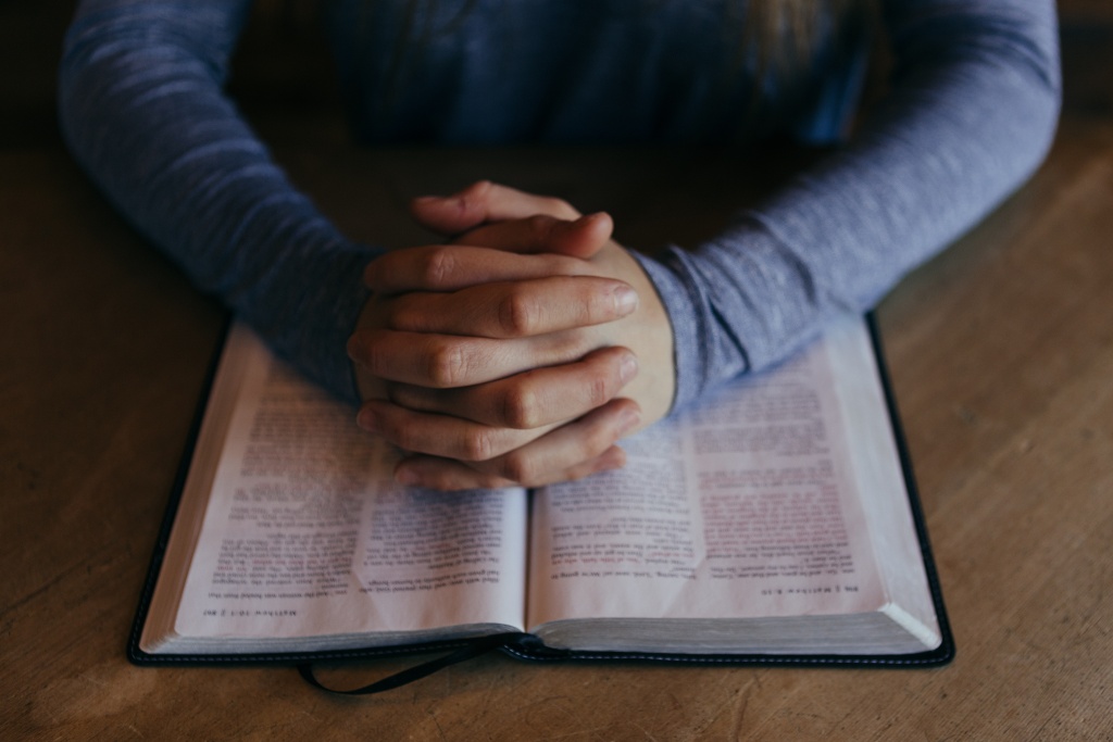 Folded hands on an open Bible