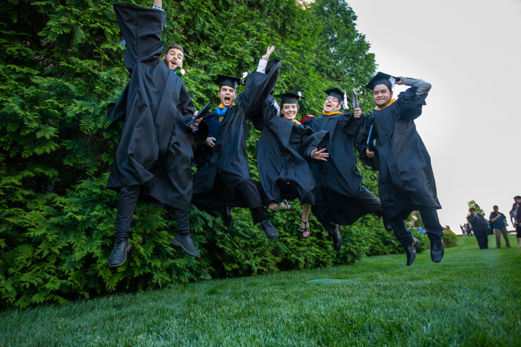 Five graduates in caps and gowns leaping for joy