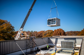 A crane lifts the new HVAC unit onto the roof (Photo by Derek Eckenroth)