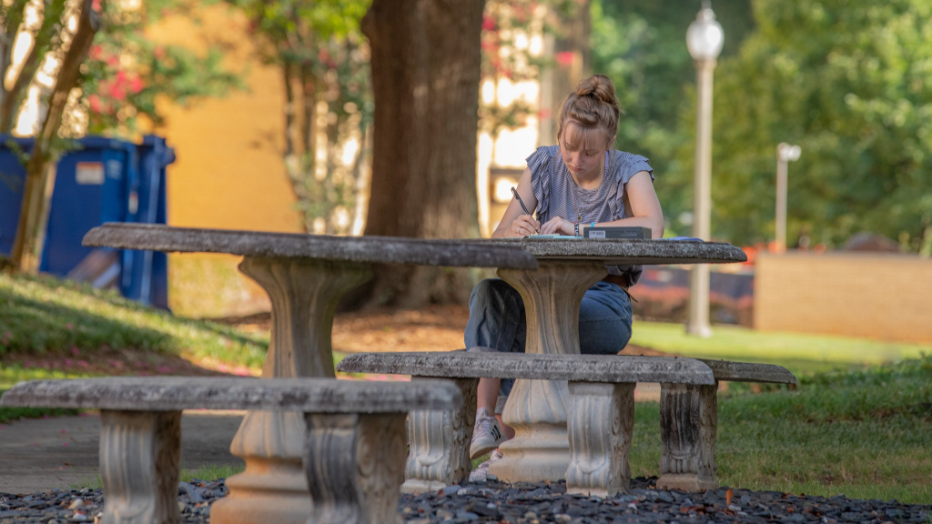 Female student studying her Bible at a table behind the girls' residence halls