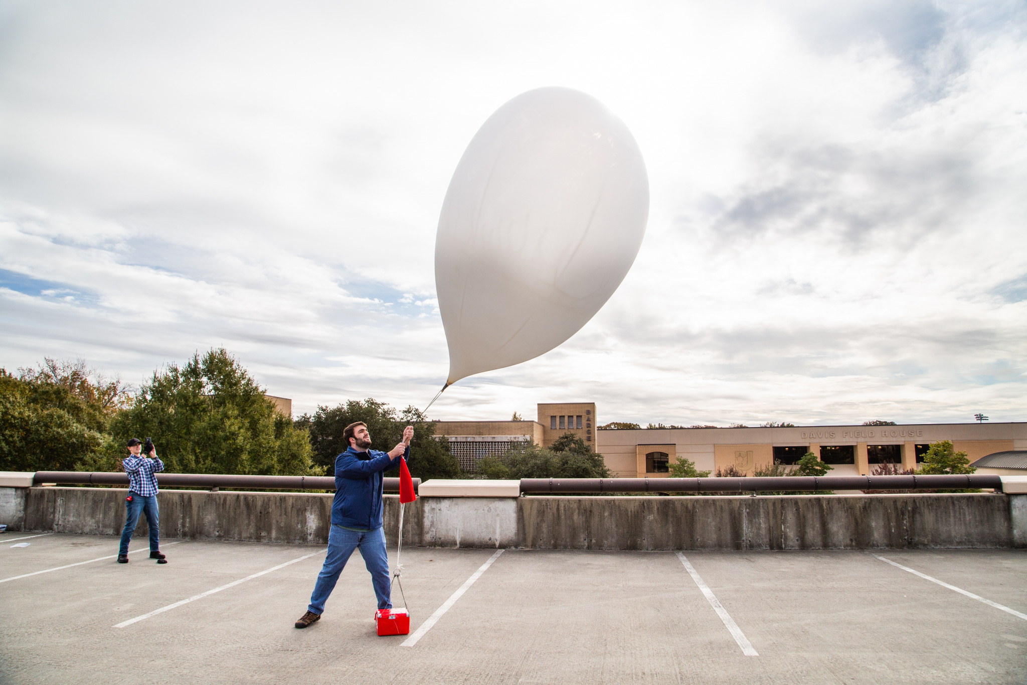 A freshman engineering student holds a weather balloon on the top of the parking garage